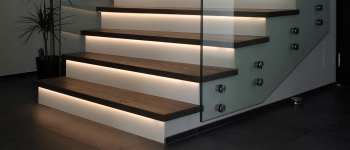 Eine Treppe mit Glasgeländer, LED-Leuchten und Produkten. T&K WOHNSTDIO - Raumausstattung, Bodenbeläge, Vinylboden, Parkett, Gardinen - Saarburger Straße 25, 67071 Ludwigshafen